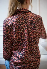 Camisa de corte clásico con cuello camisero y cierre frontal de botones. Confeccionada en seda con estampado animal print en tonos rojizos y negros, presenta mangas largas con puños abotonados y un tablón en la espalda.