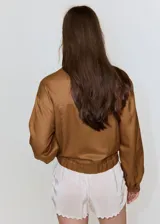 Chaqueta de diseño corto en tono tostado, confeccionada con mezcla de lyocell, algodón y lino. Presenta cuello redondo, mangas largas abullonadas, elásticos en los laterales y cierre frontal de botonadura visible.