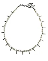 Collar de estilo punk compuesto por una alternancia de perlas de vidrio blancas y cuentas negras, intercaladas con púas metálicas plateadas. Cuenta con una cadena de ajuste de acero inoxidable.