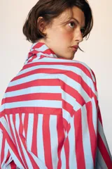 Camisa de manga larga con cuello subido y detalle de lazada frontal. Presenta un diseño de rayas verticales en tonos verde y celeste, con cierre frontal de botones y puños clásicos.