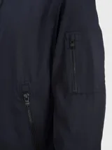 Campera bomber azul marino de poliéster con cuello alto, cierre frontal con cremallera, puños y dobladillo elásticos, dos bolsillos laterales con cremallera y un bolsillo pequeño con cremallera en la manga izquierda.