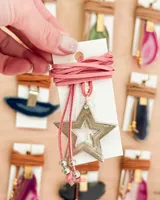 Gargantilla tipo choker con cordón de gamuza sintética color rosa y dije de estrella plateada con estrella calada en el centro.