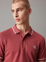 Chomba de manga corta Calvin Klein, corte slim, color rojo ladrillo con detalles de ribetes blancos en cuello y mangas. Presenta cierre frontal de dos botones y logo monograma bordado en el pecho.