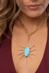 Collar corto de cadena dorada con eslabones rectangulares y un gran dije colgante en forma de sol con piedra de cristal checo turquesa en el centro.