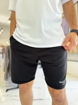 Bermuda de jogging color beige, con bolsillos laterales y estampa con texto blanco en la pierna izquierda.