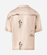 Camisa de lyocell color beige con corte boxy, cuello bowling y mangas cortas. Presenta un delicado bordado floral artesanal y cierre frontal con botones.