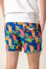 Short de baño azul vibrante con estampado repetitivo de cruces pequeñas en blanco y rojo. Presenta cintura elástica fruncida y cordón de ajuste trenzado en color coral con puntas de neón verde lima.