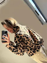 Buzo de corderito color beige con estampado animal print de leopardo en negro. Tiene cuello alto con cierre de cremallera y bolsillo tipo parche en el pecho de tela lisa color negro.