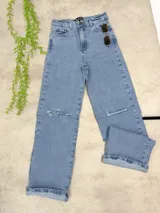 Pantalón de jean estilo wide leg en color azul claro, con diseño de tiro alto y corte relajado. Presenta detalles de roturas en ambas rodillas y ruedos doblados.