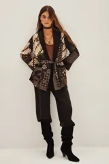 Saco tipo kimono con estampado batik en tonos marrones y negros, con solapas lisas, mangas largas y lazo ajustable en la cintura. Incluye bolsillos frontales y forro interior.