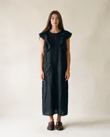 Vestido midi de lino negro con bolsillos delanteros, volados en los hombros y costuras pespunteadas en contraste. Presenta un corte holgado y cuello redondo.