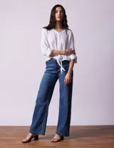 Blusa blanca de algodón marca Dash, con escote en V, abertura con botones, mangas 3/4 regulables con presilla y botón, y terminación de ruedo anudado.