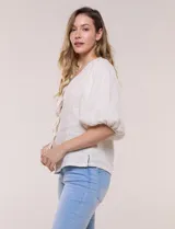 Blusa color beige confeccionada en lino, con escote en V pronunciado y cierre frontal de múltiples lazos para atar. Presenta mangas abullonadas tres cuartos con puños elásticos y corte relajado.