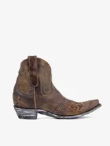 Bota corta estilo cowboy de cuero marrón desgastado, con punta afilada y tacón bajo. Presenta bordados en hilo dorado en el empeine y caña, incluyendo un diseño de estrellas troqueladas en la puntera. El tacón tiene un acabado envejecido plateado.