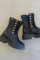 Borcego de caña corta confeccionado en cuero negro, con diseño de cordones y ganchos metálicos, cierre lateral y suela de plataforma dentada.