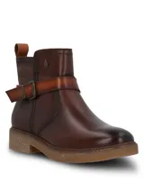Botines de cuero color marrón oscuro, con diseño de caña media, cierre lateral y una tira decorativa con hebilla metálica sobre el empeine. Presentan una suela de goma texturizada en tono natural y un pequeño logo metálico en la parte superior de la caña.