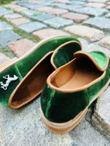 Mocasines de terciopelo verde oscuro, con ribetes en tono tostado y detalle de aplique metálico de un caballito en el talón. Poseen suela y taco bajo de madera.