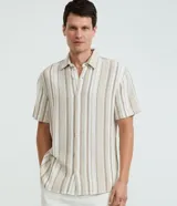 Camisa de manga corta para hombre, confeccionada en algodón con textura, cuello inglés y cierre frontal de botones. Presenta un diseño de rayas verticales en tonos beige y blanco.