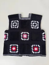 Chaleco sin mangas, confeccionado con cuadrados de cuero negro perforado combinados con cuadrados de crochet en hilo de algodón negro y blanco, con detalles centrales en rojo.
