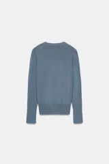 Jersey de punto liso color negro, con cuello redondo y manga larga. Presenta una hilera de cuatro botones dorados decorativos en el puño de cada manga.