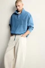 Camisa polo de corte relajado confeccionada en denim ligero de algodón con efecto lavado. Presenta cuello subido, cierre frontal con botonadura oculta por solapa, manga larga, bolsillo de plastrón en el pecho y bajo ajustable con cordón.