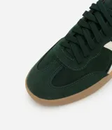 Championes de estilo retro tipo chuteira, color verde oscuro con detalles en blanco crema y suela de goma color caramelo. Presentan un acabado con efecto gamuza y cierre mediante cordones.