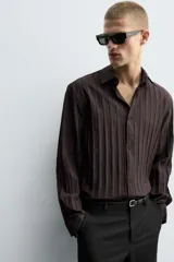 Camisa de manga larga con ajuste relajado, confeccionada en tejido de viscosa con textura de rayas verticales. Presenta cuello camisero, cierre frontal de botones y aberturas en el bajo lateral.