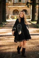 Poncho tejido de lana merino color negro, con cuello alto, diseño amplio y flecos en el ruedo. Presenta detalles de bordados circulares en color crudo y apliques de flecos decorativos en los laterales.