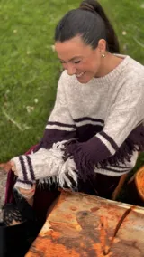 Sweater de punto con diseño de bloques de color en tonos beige y bordó, con cuello redondo, mangas largas y detalle de flecos decorativos en el cuerpo y las mangas.