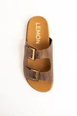 Sandalias de cuero marrón, con dos tiras anchas ajustables mediante hebillas metálicas doradas. Cuenta con una suela de corcho y base dentada.