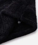 Buzo de felpa sintética tipo corderito negro con cuello alto, cierre frontal parcial, bolsillo tipo canguro y etiqueta aplicada en el pecho.