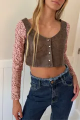 Top corto confeccionado en cuero negro con mangas largas de encaje floral. Presenta escote en V, diseño entallado con costuras decorativas y cierre frontal mediante botones metálicos.