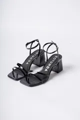 Sandalias de tacón cuadrado medio, color negro con acabado brillante, diseño de tiras finas en el empeine y cierre de pulsera con hebilla al tobillo.