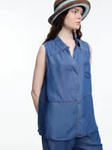 Camisa sin mangas en denim 100% lyocell, muy liviano con caída fluida. De corte recto y largo medio, presenta cartera escondida en el frente y un bolsillo plaqué en el pecho. En la espalda, un detalle distintivo: botones decorativos alineados en abertura vertical. Los pespuntes a contratono completan el look.