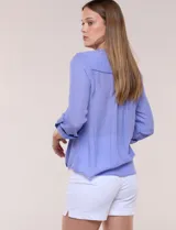 Blusa violeta de corte fluido, con cuello mao, escote en V y bolsillo plaqué en el pecho. Presenta mangas largas regulables con presilla y un lazo frontal para anudar en la cintura.