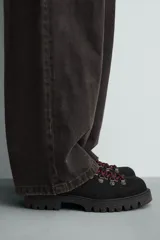 Zapato de cordones estilo trekking para hombre, confeccionado en piel con acabado de serraje color marrón. Presenta enganches metálicos para los cordones, cuello acolchado en color negro y una suela de goma con volumen y efecto moteado.