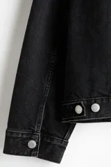 Campera trucker de denim rígido en color negro, con cuello camisero, cierre frontal de botones metálicos, bolsillos con solapa en el pecho y bolsillos laterales.