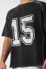 Remera de algodón con estilo deportivo, color verde oliva con efecto de lavado gastado. Presenta el número 15 estampado en blanco en el frente y detalles de costuras con vivos blancos en los hombros. Posee cuello redondo y corte holgado.