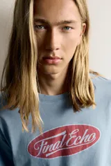 Remera relaxed fit color celeste con efecto lavado, de manga corta y cuello redondo. Presenta un estampado frontal con la inscripción "Final Echo" en el interior de un ovalo rojo.