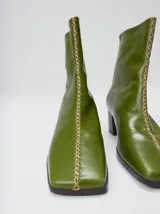 Botas de caña media color marrón, confeccionadas en cuero con acabado brillante. Presentan punta cuadrada, taco de madera y un distintivo bordado decorativo en color rojo que recorre el empeine hasta la punta.