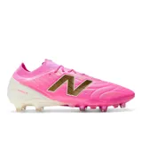 Championes de fútbol New Balance modelo Tekela, color fucsia con detalles en blanco y logo dorado. Presentan un diseño de corte bajo con estructura tejida y suela con tapones para césped natural.