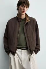 Cazadora bomber reversible de corte relaxed fit, color marrón oscuro, con cuello alto, cierre frontal de cremallera, bolsillos laterales de vivo y acabados elásticos en puños y dobladillo.