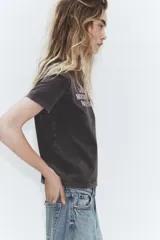Camiseta de algodón con efecto lavado, cuello redondo y manga corta. Presenta un estampado frontal con texto en color claro.