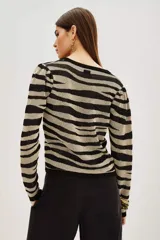 Sweater de tejido de punto con cuello redondo y manga larga, presentando un estampado de rayas negras y beige metalizado con efecto cebra.