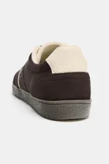 Zapatillas deportivas de gamuza en color marrón oscuro, con detalles de franjas laterales en color crema y refuerzo en el talón. Presentan cierre mediante cordones y suela de goma texturizada.