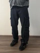 Pantalón tipo jean cargo de corte baggy, color negro lavado, con múltiples bolsillos laterales con solapa.