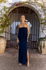 Vestido largo azul marino sin mangas, de corte recto con tajo lateral y diseño strapless con sobrecapa fluida superpuesta.
