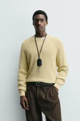 Sweater de punto canalé color beige, con cuello redondo y mangas largas con diseño raglán.