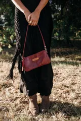 Mini cartera de cuero color bordó, con cierre superior, correa fina desmontable y bolsillo interior con cierre.