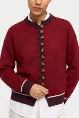 Saco tejido de punto color bordó con cierre frontal de alamares y botones. Presenta detalles en color contraste en cuello, puños y ruedo, con una línea fina en tono claro.